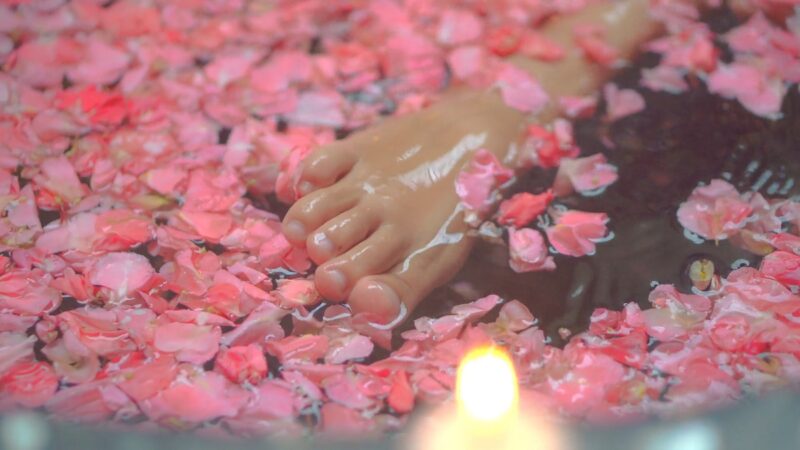 A close-up of a foot soaking in a warm spa bath filled with pink flower petals