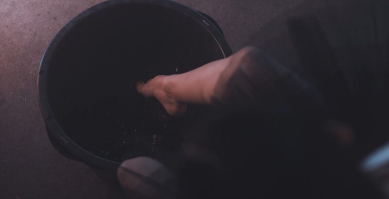 A person soaking their foot in a dark bucket of water, likely for a foot treatment or relaxation